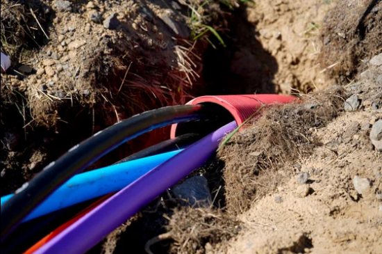 Blue, purple and black utility cables emerging from a red duct in a trench