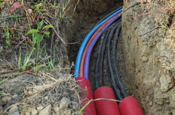 Coloured utility ducts and cables buried together in a trench